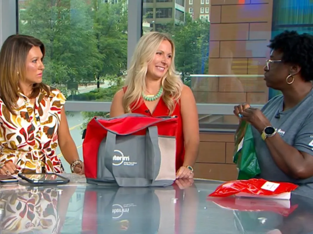 Your Carolina TV Show female host stands at table beside Interim HealthCare two female employees doing a demonstration on medication management.
