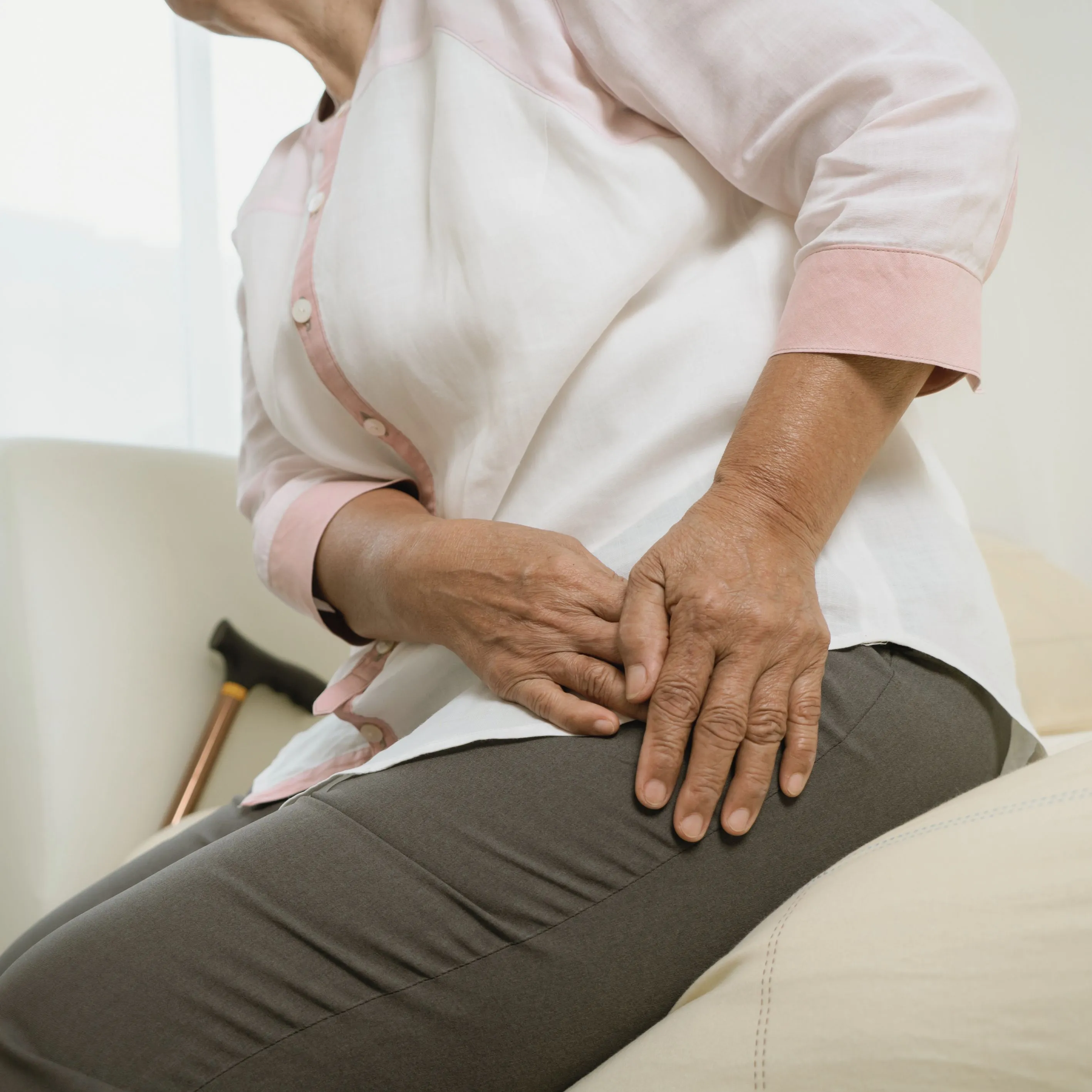 Older woman sitting on couch while grasping at hip joint.